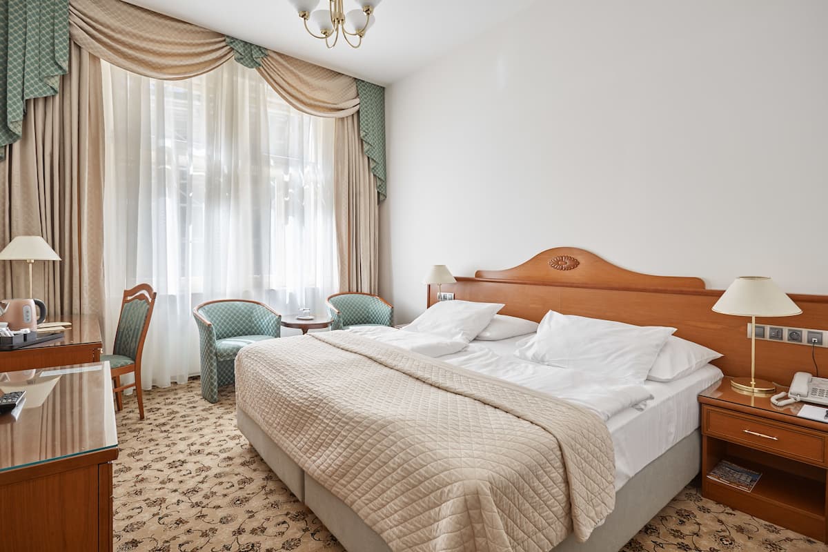 Ein Hotelzimmer mit einem großen Bett, zwei Stühlen, einem Schreibtisch und einem Nachttisch mit Lampe und Telefon.