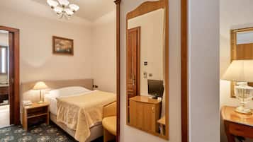 Habitación de hotel con cama, mesita de noche con lámpara, espejo, un cuadro en la pared y alfombra estampada.
