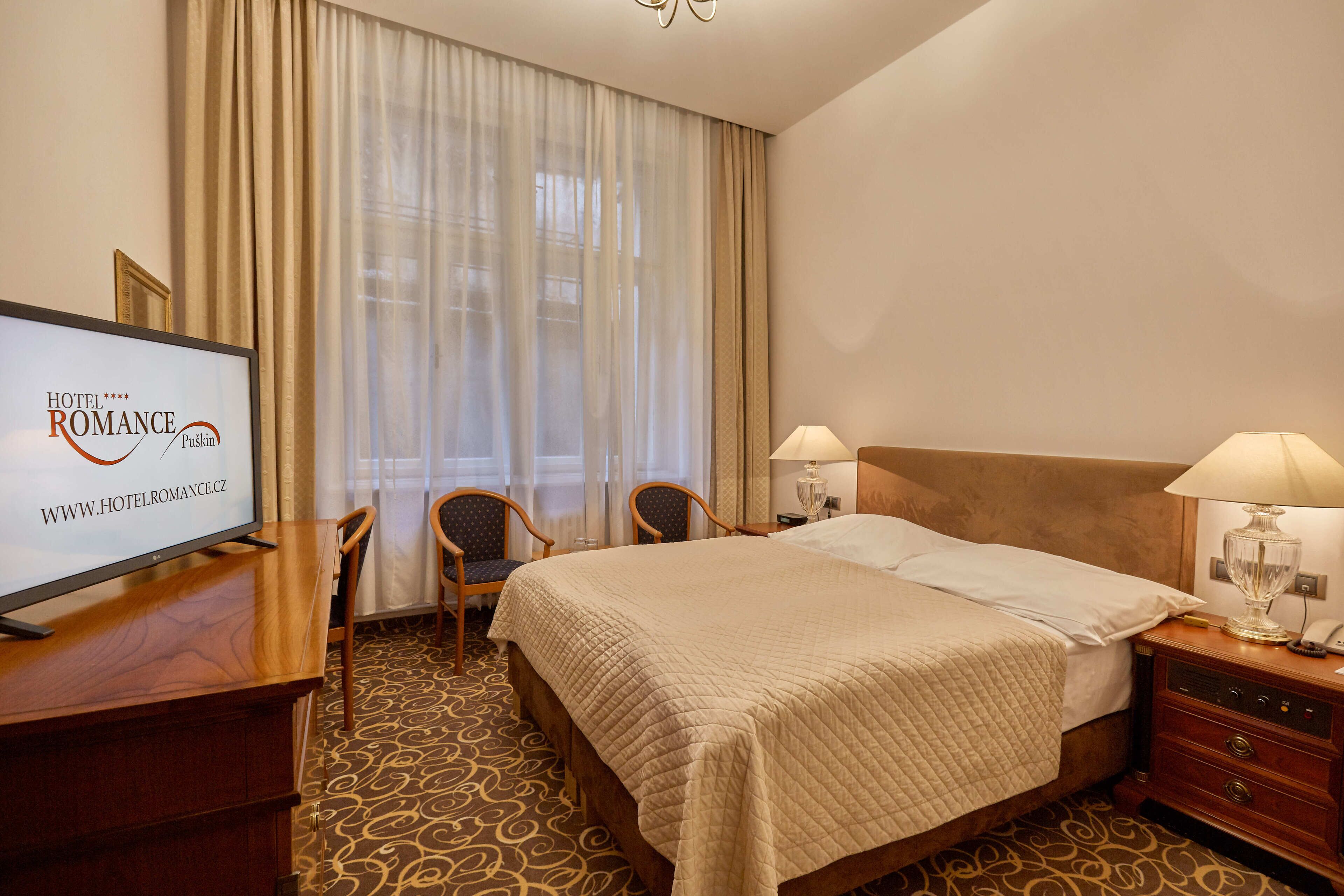 A hotel room with a bed, two bedside tables with lamps, a desk with a television, and a chair.