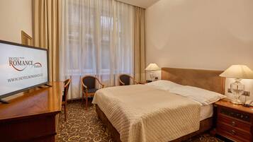 A hotel room with a bed, two bedside tables with lamps, a desk with a television, and a chair.