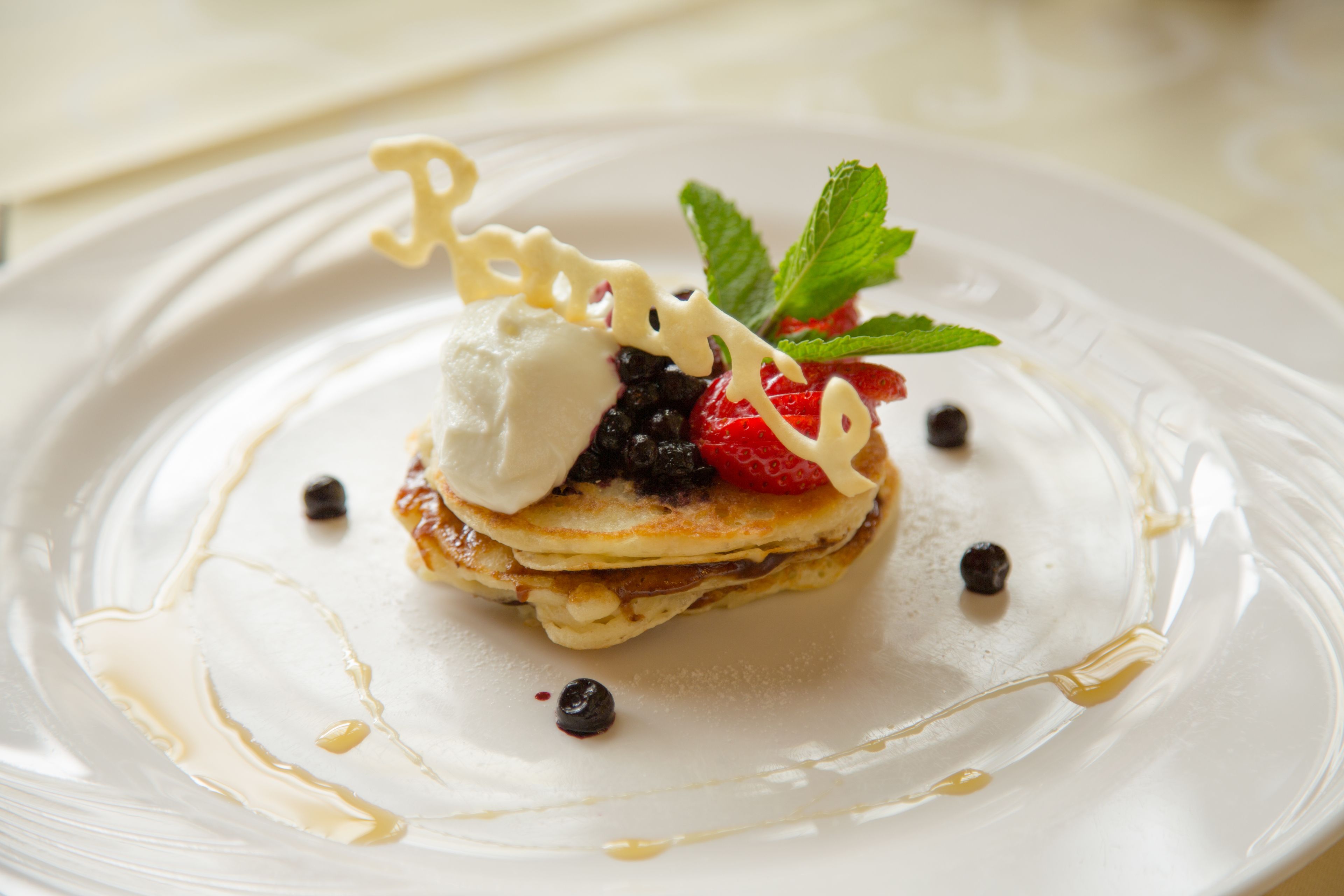 A dessert with a dollop of cream, a strawberry, and a mint leaf on a white plate.