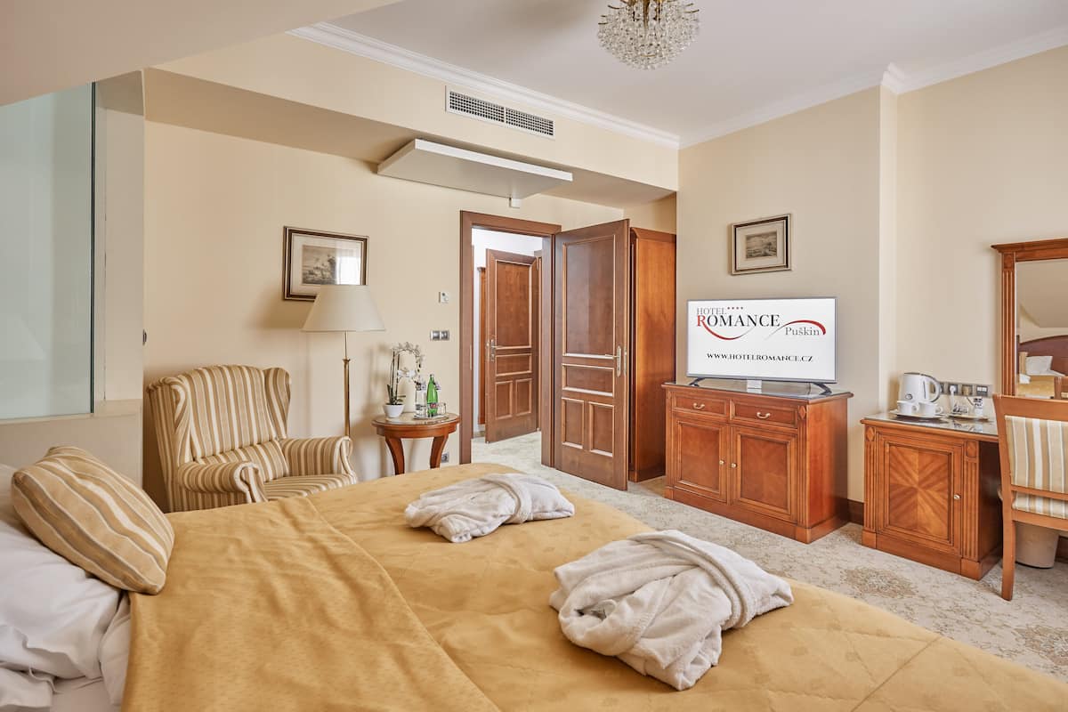 Ein Hotelzimmer mit einem großen Bett, einem Fernseher, einem Schreibtisch mit Kaffeemaschine und einem Sessel.