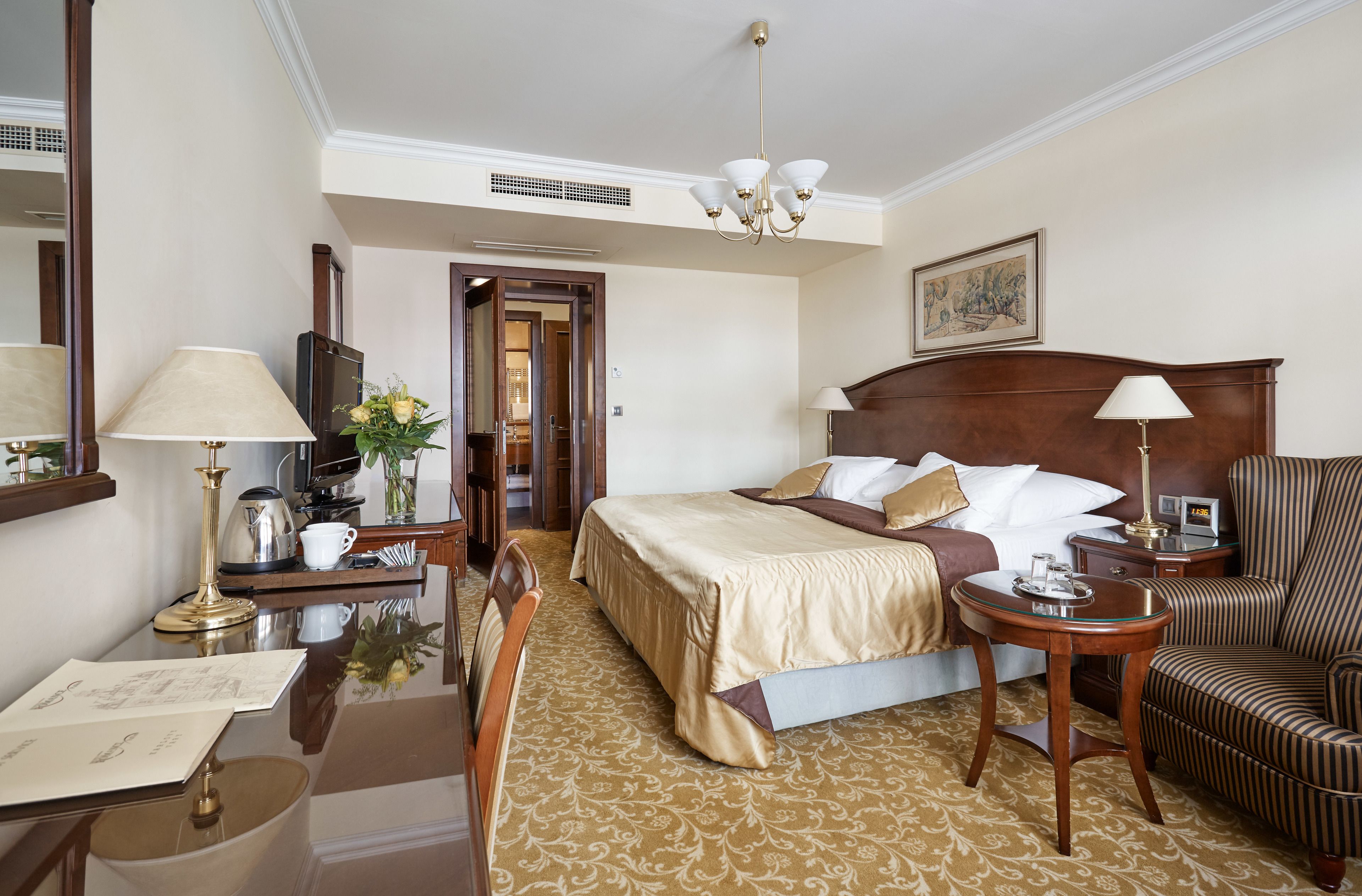 Habitación de hotel con una cama grande, un área de descanso con una silla, un escritorio con lámpara y un televisor.