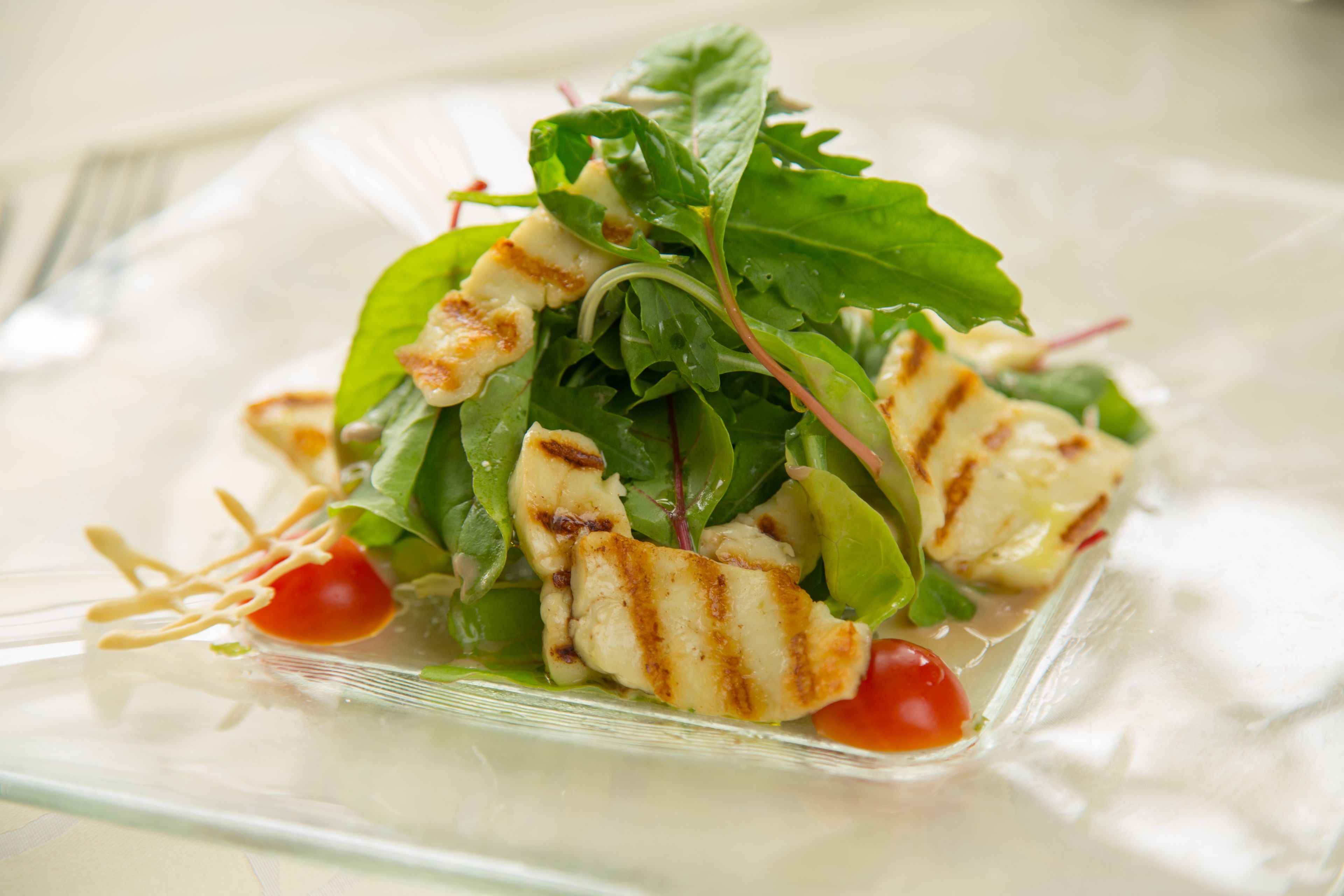 Ensalada con pollo a la parrilla y vegetales sobre un plato de vidrio transparente.