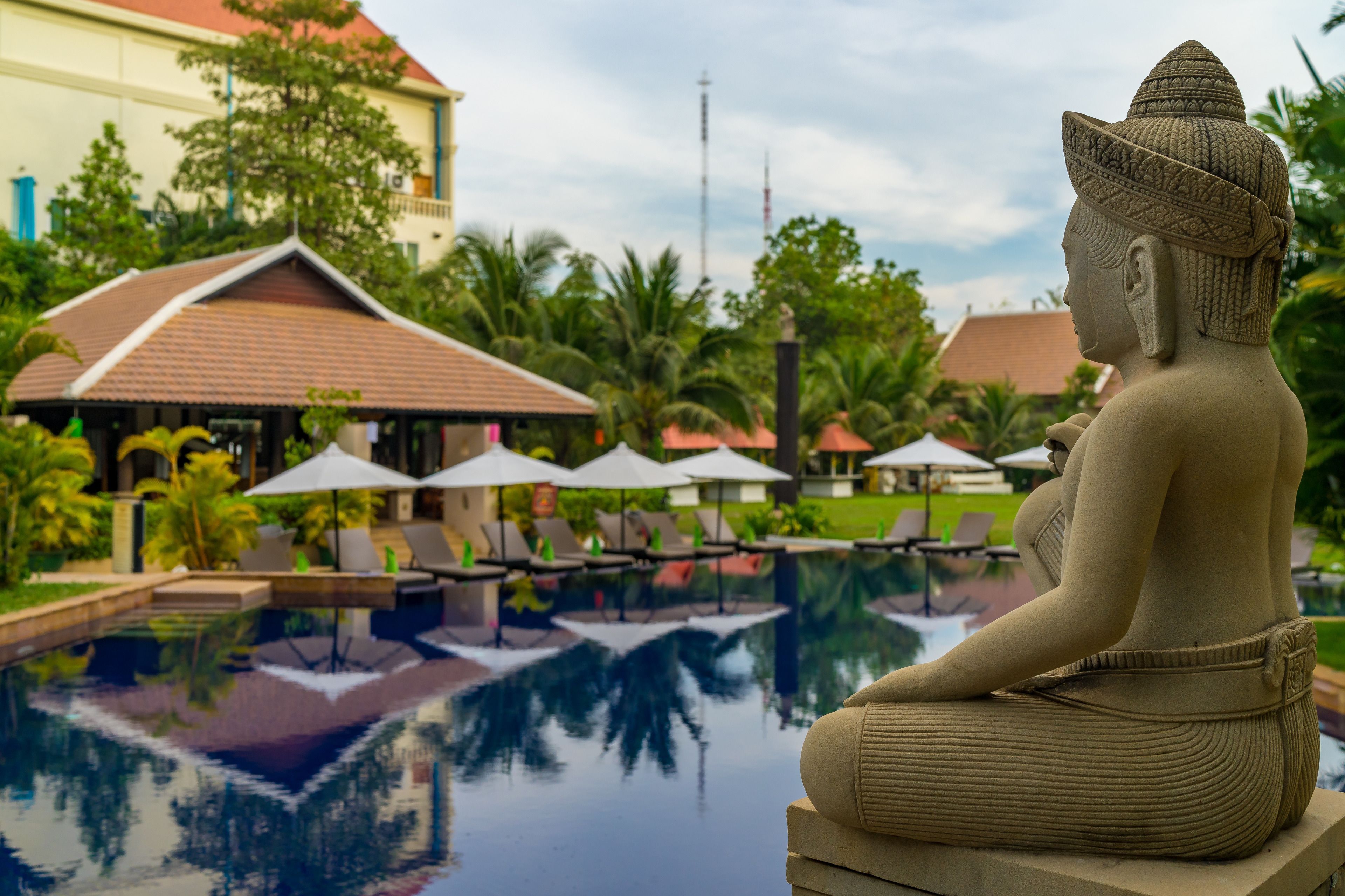Una estatua de Buda junto a una piscina con sillones de descanso y sombrillas al fondo.