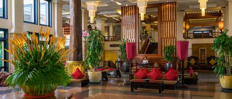A spacious lobby with a checkered floor, large potted plants, and a staircase leading to an upper level.