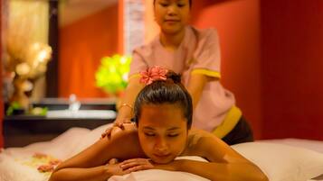 A massage therapy session in a room with a bed, pillows, and a massage table.