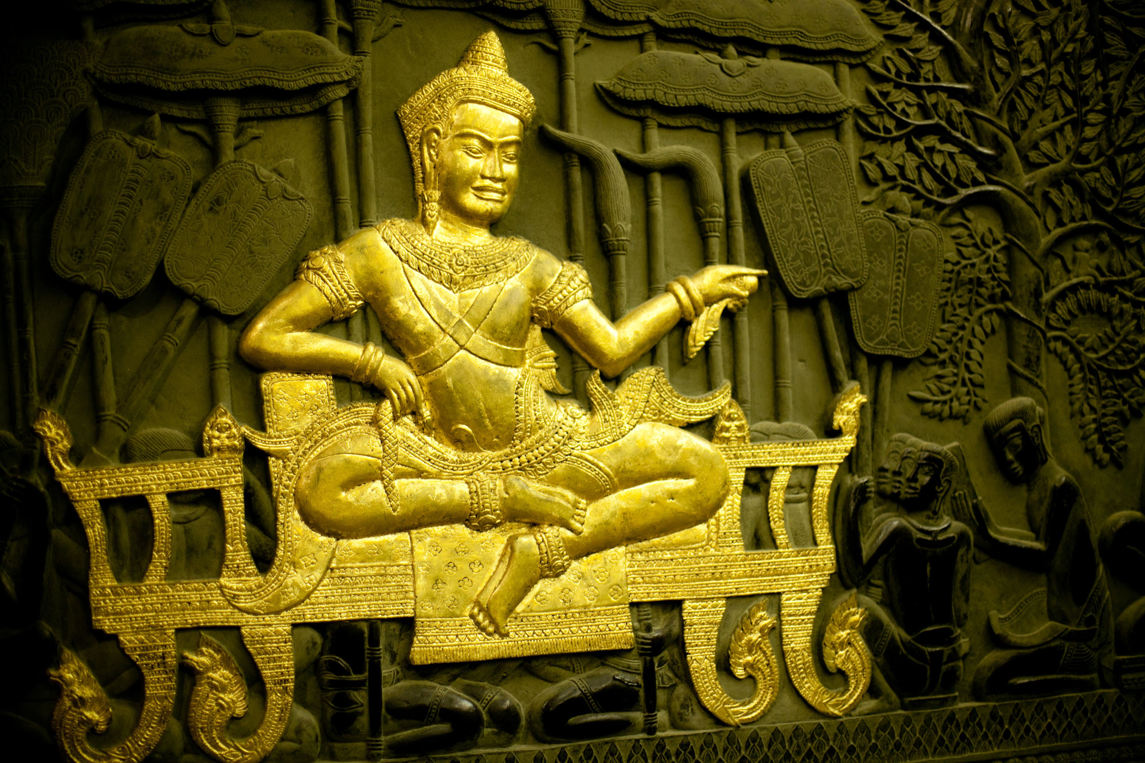 Escultura detallada de una figura sentada en pose tradicional, rodeada de tallas y diseños intrincados.