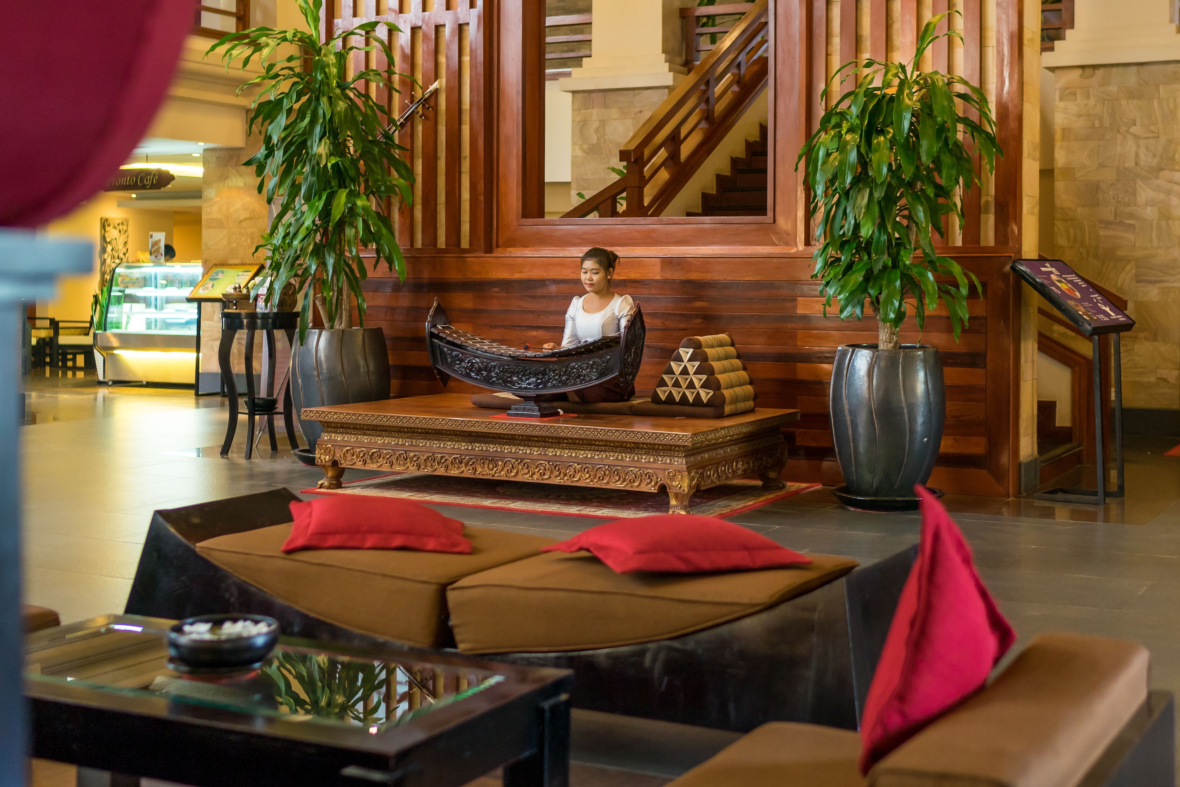 A lobby with a central seating area, large potted plants, and a staircase in the background.