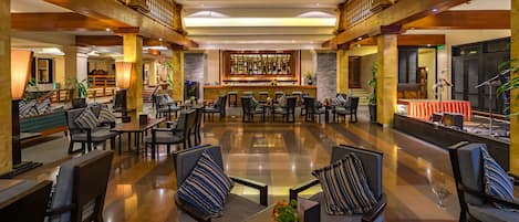 Un vestíbulo amplio con zona de bar, arreglos de asientos y escenario para eventos.