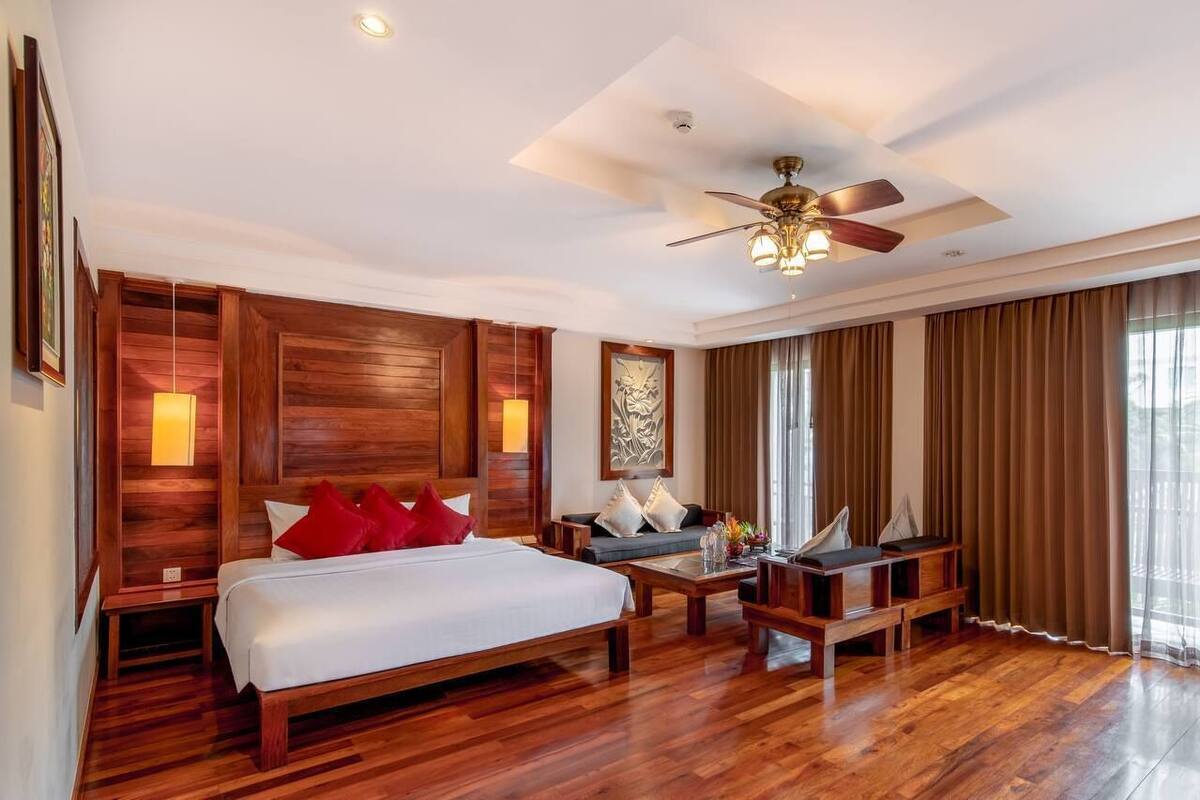A hotel room with a wooden bed, a sofa, a coffee table, and a ceiling fan.