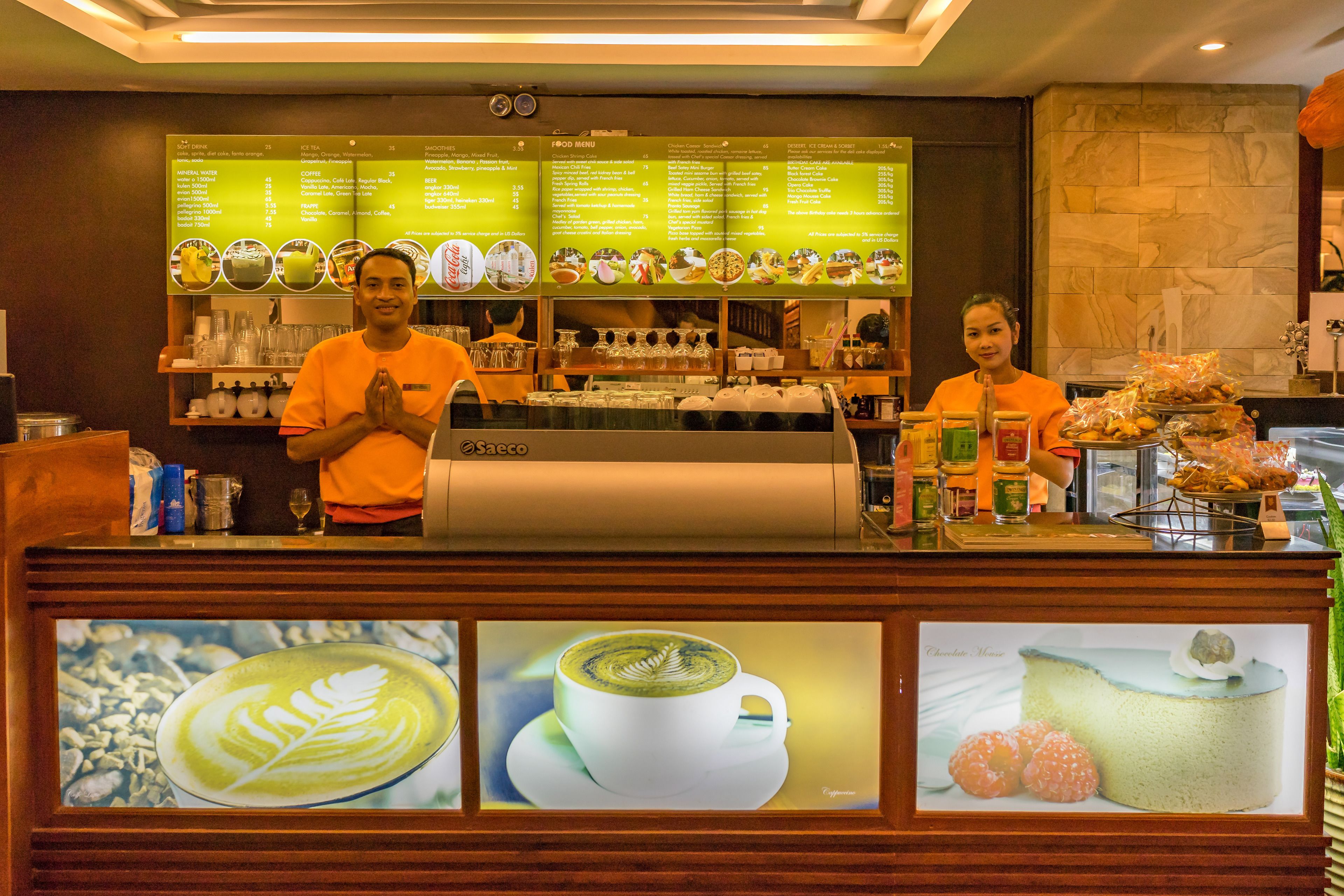 A coffee shop counter with a menu board, a coffee machine, and a display of pastries.
