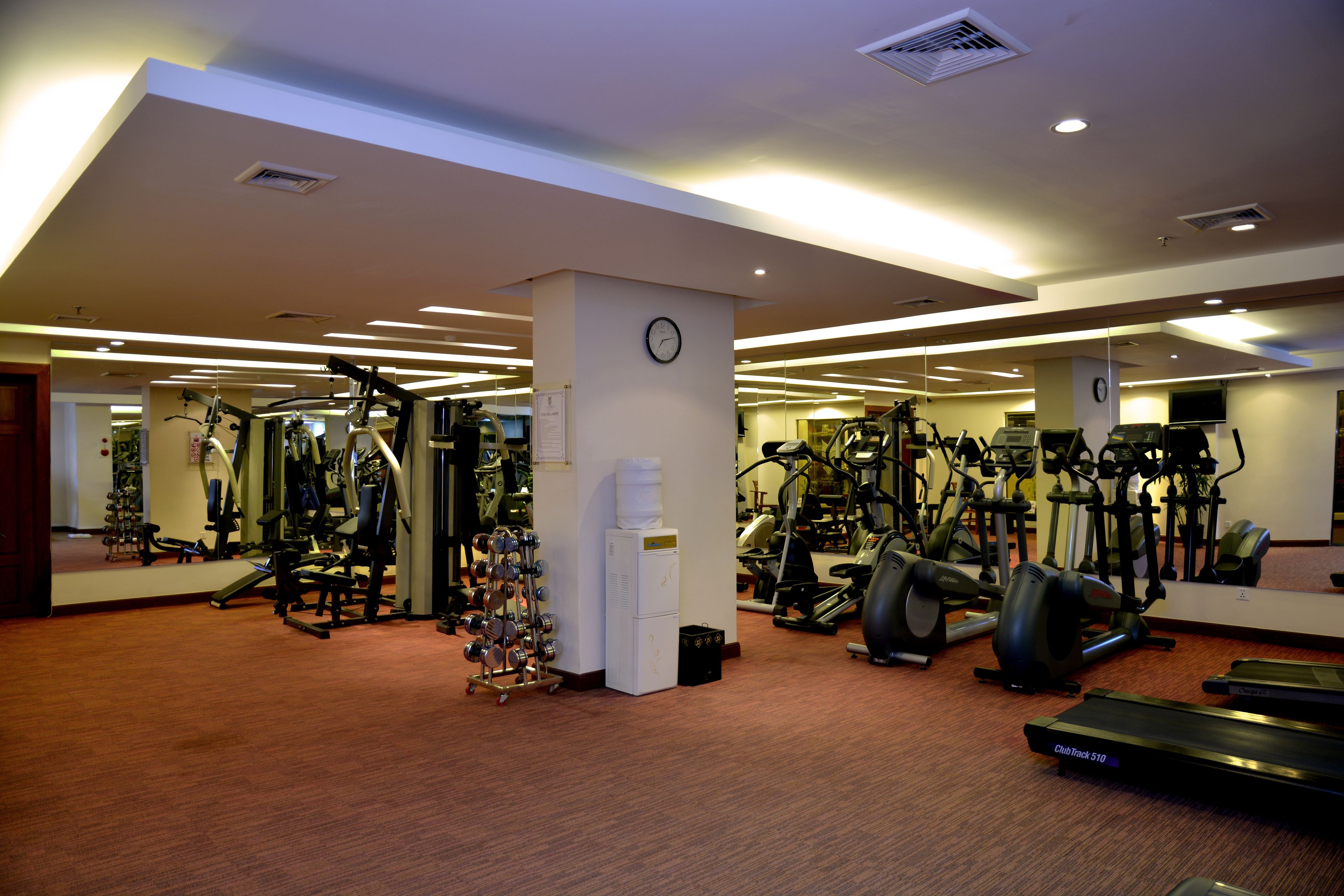 Une salle de sport équipée de divers appareils d’exercice, notamment des tapis de course, des vélos d’appartement et des appareils de musculation.