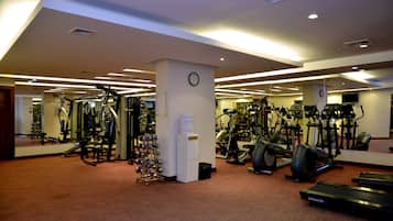 Een fitnessruimte met diverse trainingsapparaten, waaronder loopbanden, hometrainers en krachttoestellen.