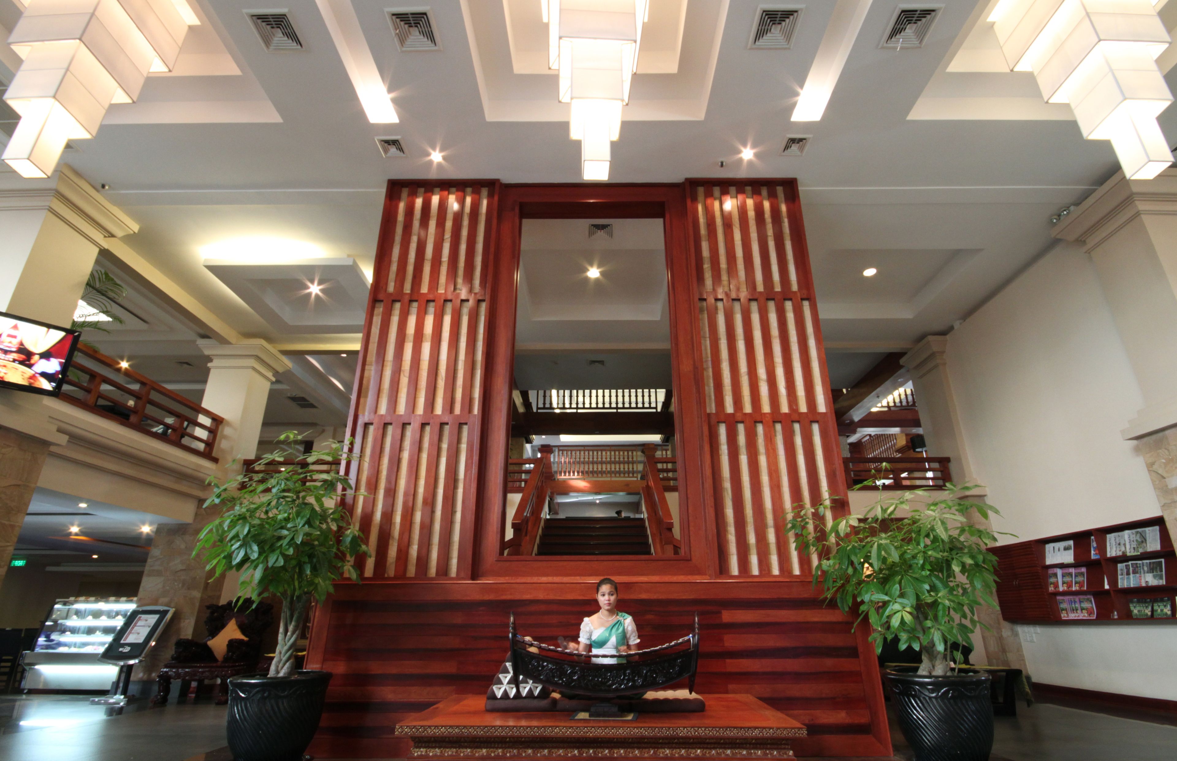 A lobby with a central staircase, potted plants, and a television screen.