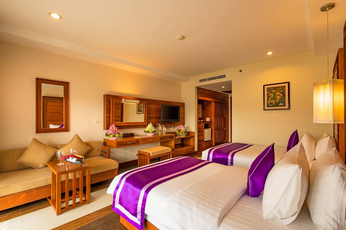 A hotel room with two beds, a sofa, a desk, and a television.
