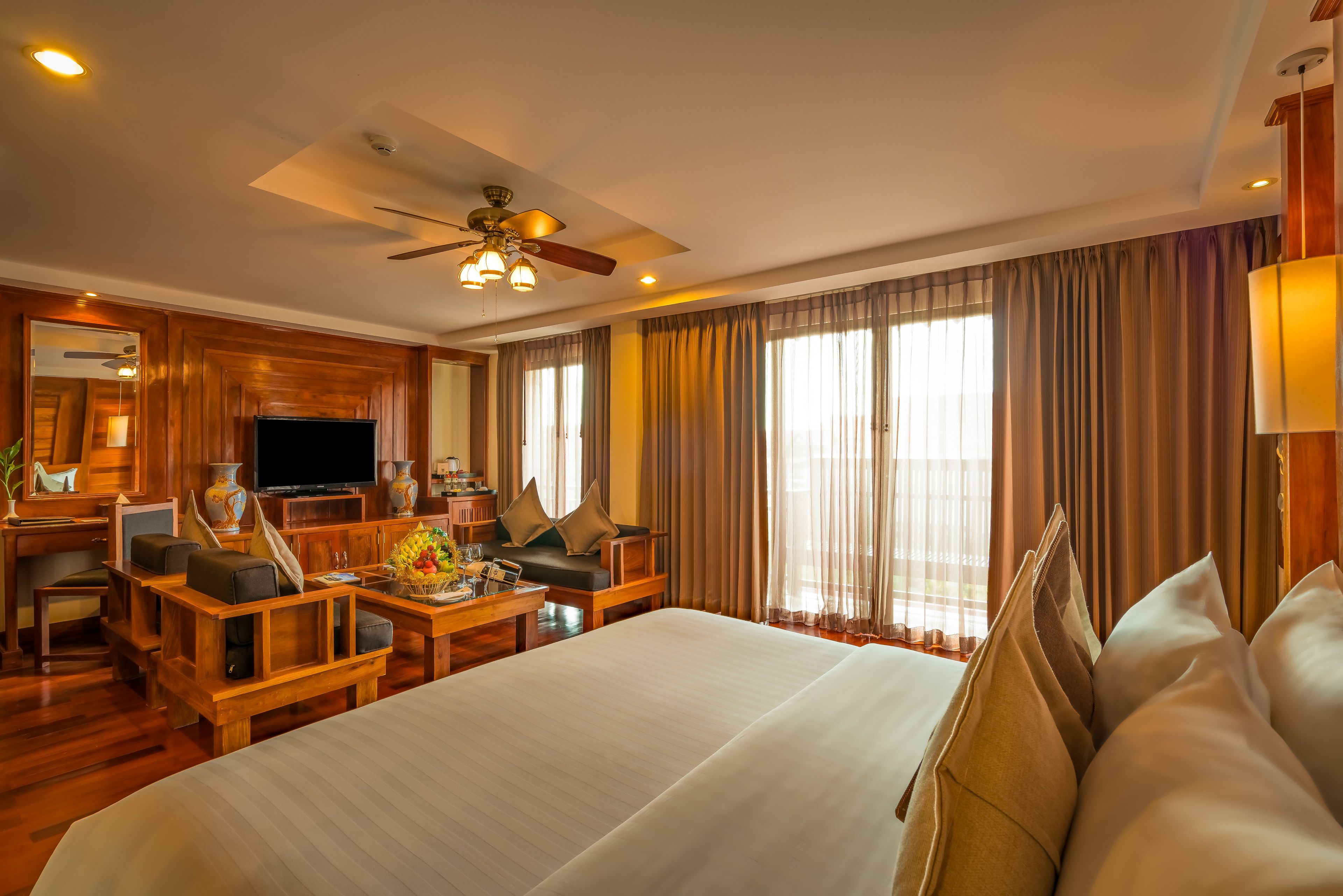 Ein Hotelzimmer mit einem großen Bett, einem Schreibtisch mit Flachbildfernseher, einer Couch und einem Deckenventilator.