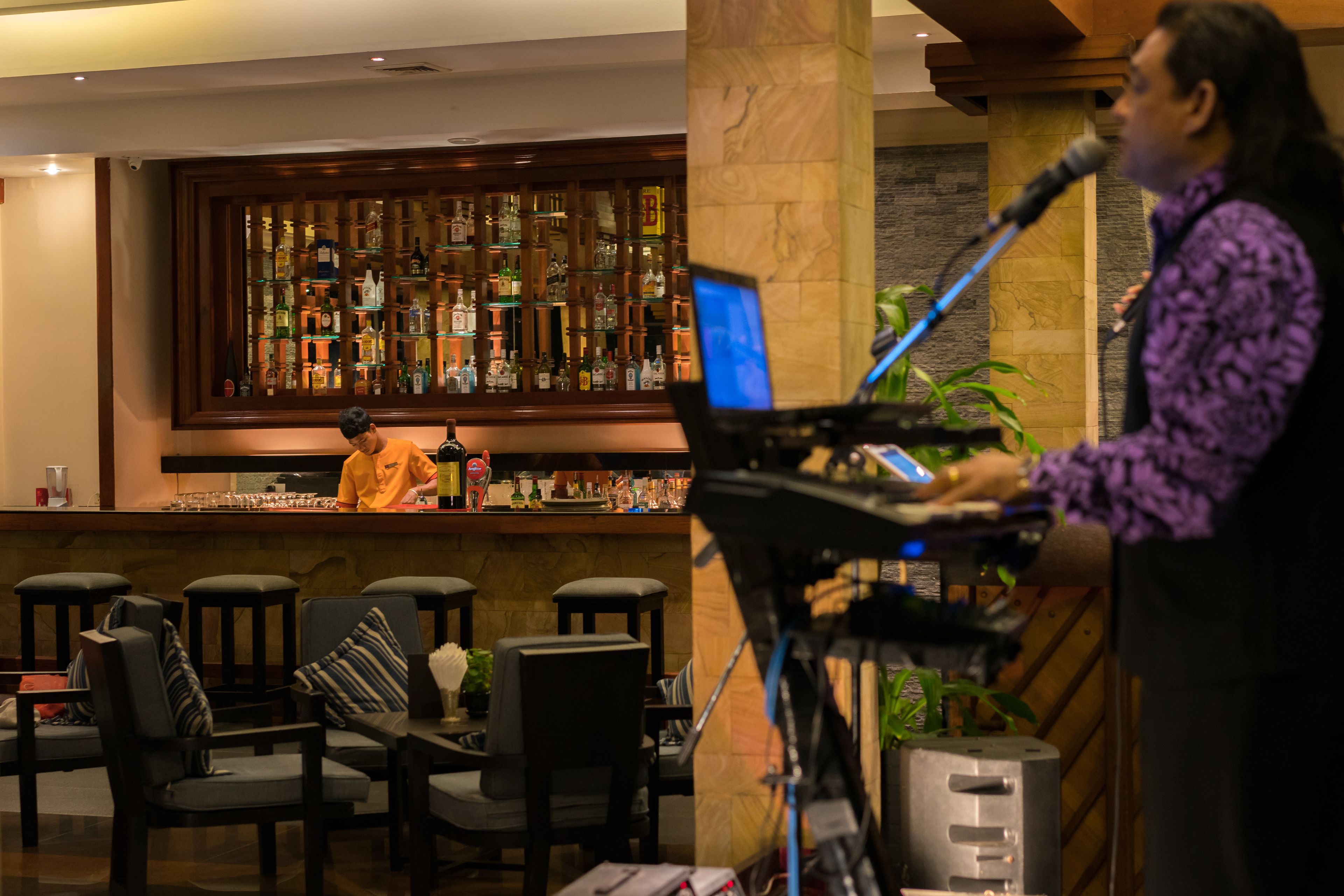 A bar area with a bartender, a piano, and several chairs.