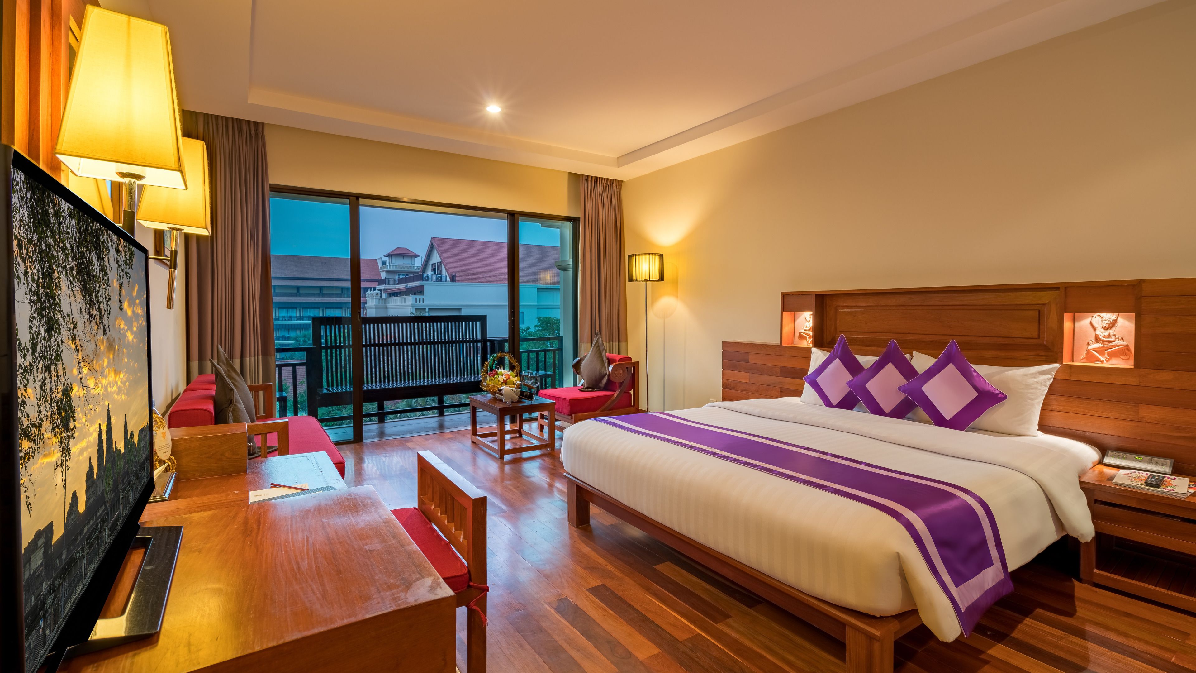 Una habitación de hotel con una cama grande, un escritorio, una silla, un balcón con vistas a edificios y un cuadro de un paisaje.