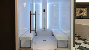 A modern shower enclosure with glass doors, a bench, and a control panel.