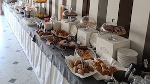 A buffet setup with various food items and glassware on a long table, set against a striped wall.