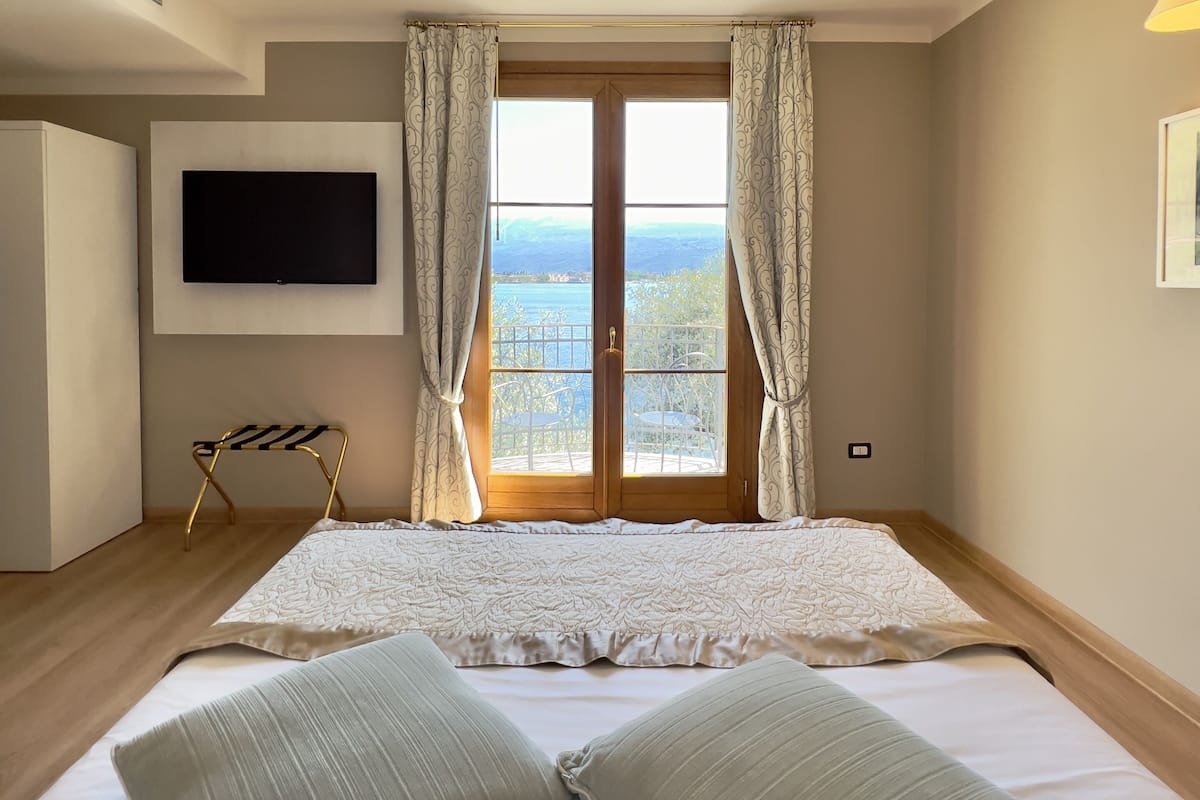 Une chambre à coucher avec un grand lit, un téléviseur fixé au mur et une fenêtre avec des rideaux.