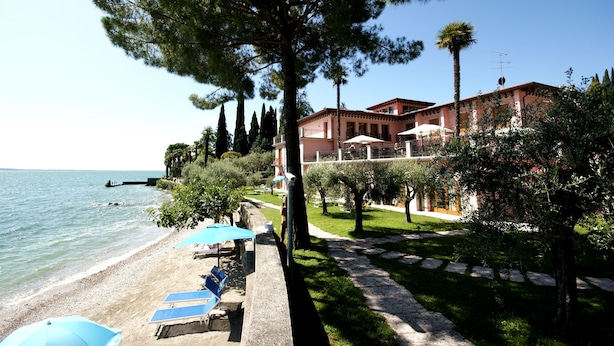 A beachside hotel with a pool area, a pathway leading to the building, and a view of the sea.