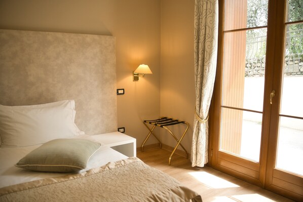 Une chambre à coucher comprenant un lit, une table de chevet, une lampe fixée au mur, une fenêtre avec des rideaux et une porte en bois.