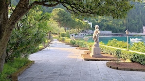 A paved pathway lined with benches and a statue, leading to a body of water with boats.