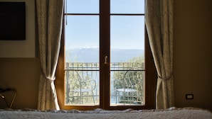 A room with a large window, curtains, a bed, and a chair.