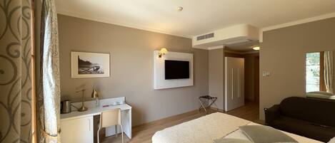 A hotel room with a bed, a desk with a chair, a television mounted on the wall, and a window.