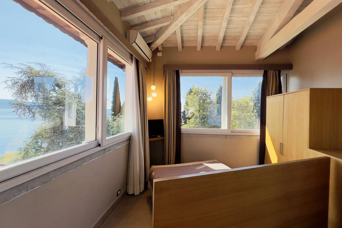 Une chambre avec un plafond en bois, de grandes fenêtres, un lit, une armoire et un téléviseur.