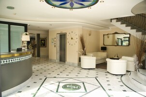 A hotel lobby with a reception desk, a clock, a staircase, and a seating area.