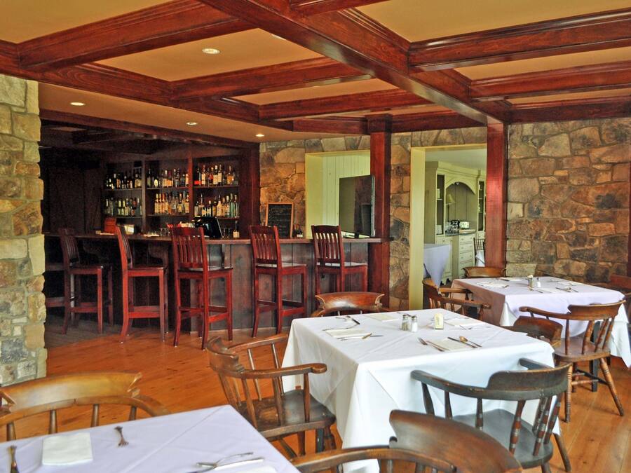 Un restaurant avec des tables et des chaises en bois, des murs en pierre et un bar avec des étagères remplies de bouteilles.