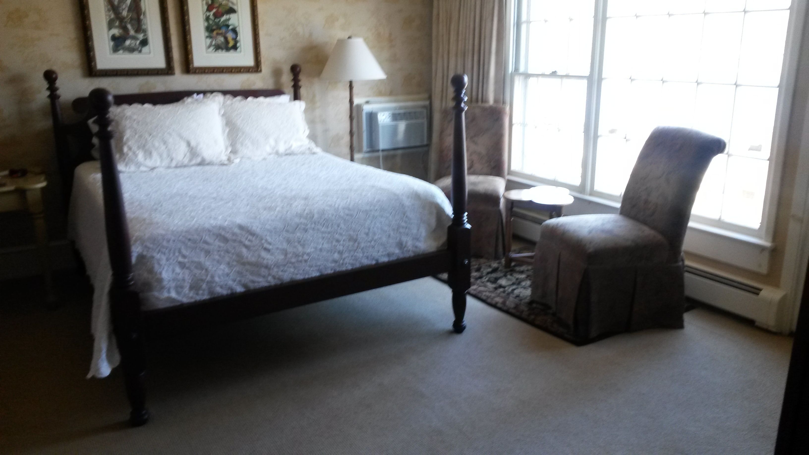 A bedroom with a four-poster bed, a chair, a lamp, and a window with curtains.