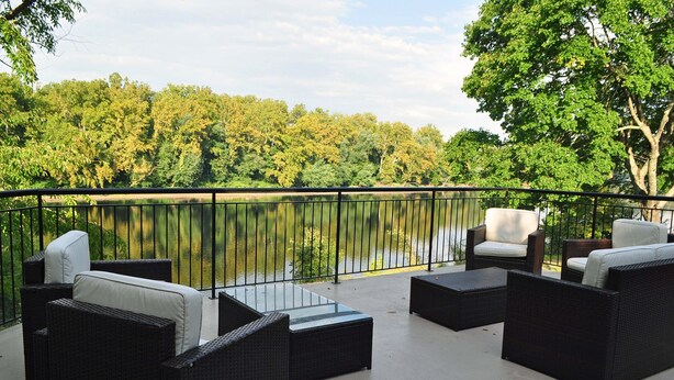 An outdoor patio with wicker furniture and a view of a lake surrounded by trees. - Lumberville 1740 House (New Hope)