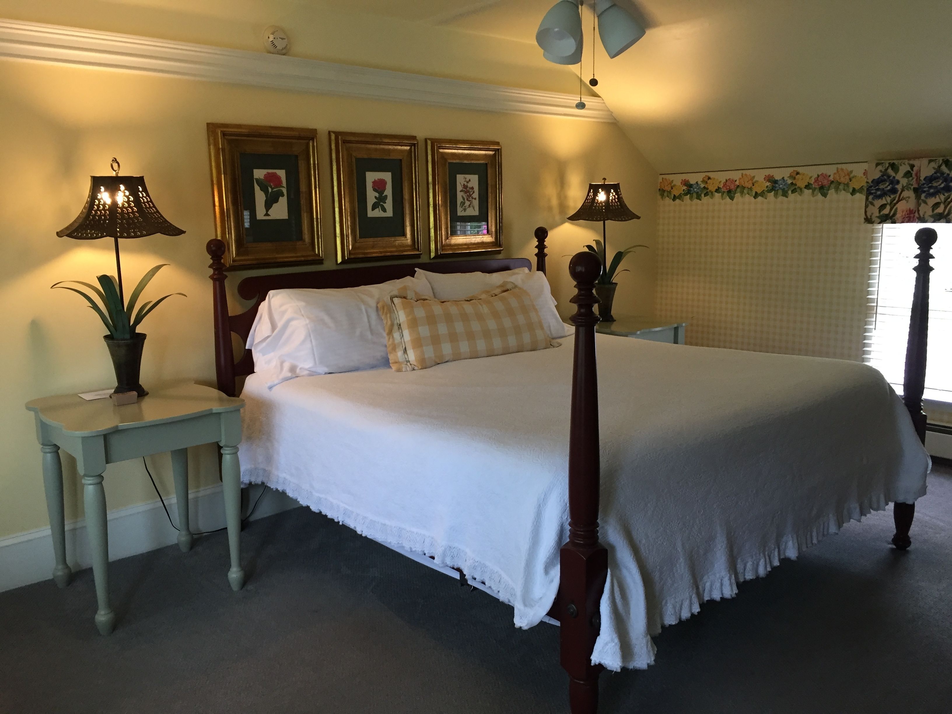 A neatly made bed with a wooden headboard, two bedside tables with lamps, and a floral-patterned window blind.