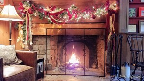 A fireplace with a Christmas garland, a leather sofa, and a metal chair. - Lumberville 1740 House (New Hope)