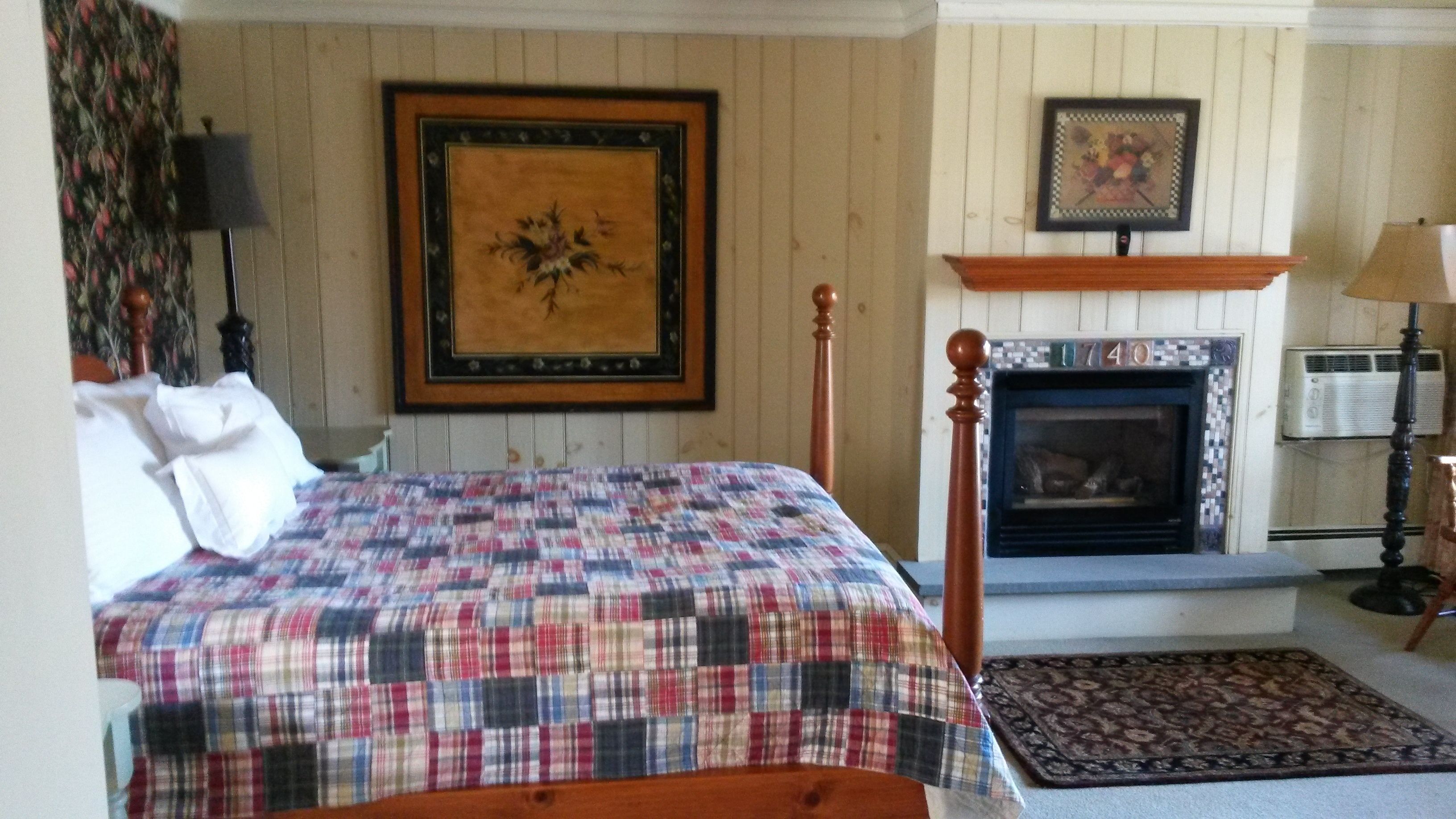 A bedroom with a bed, a fireplace, and a framed picture on the wall.