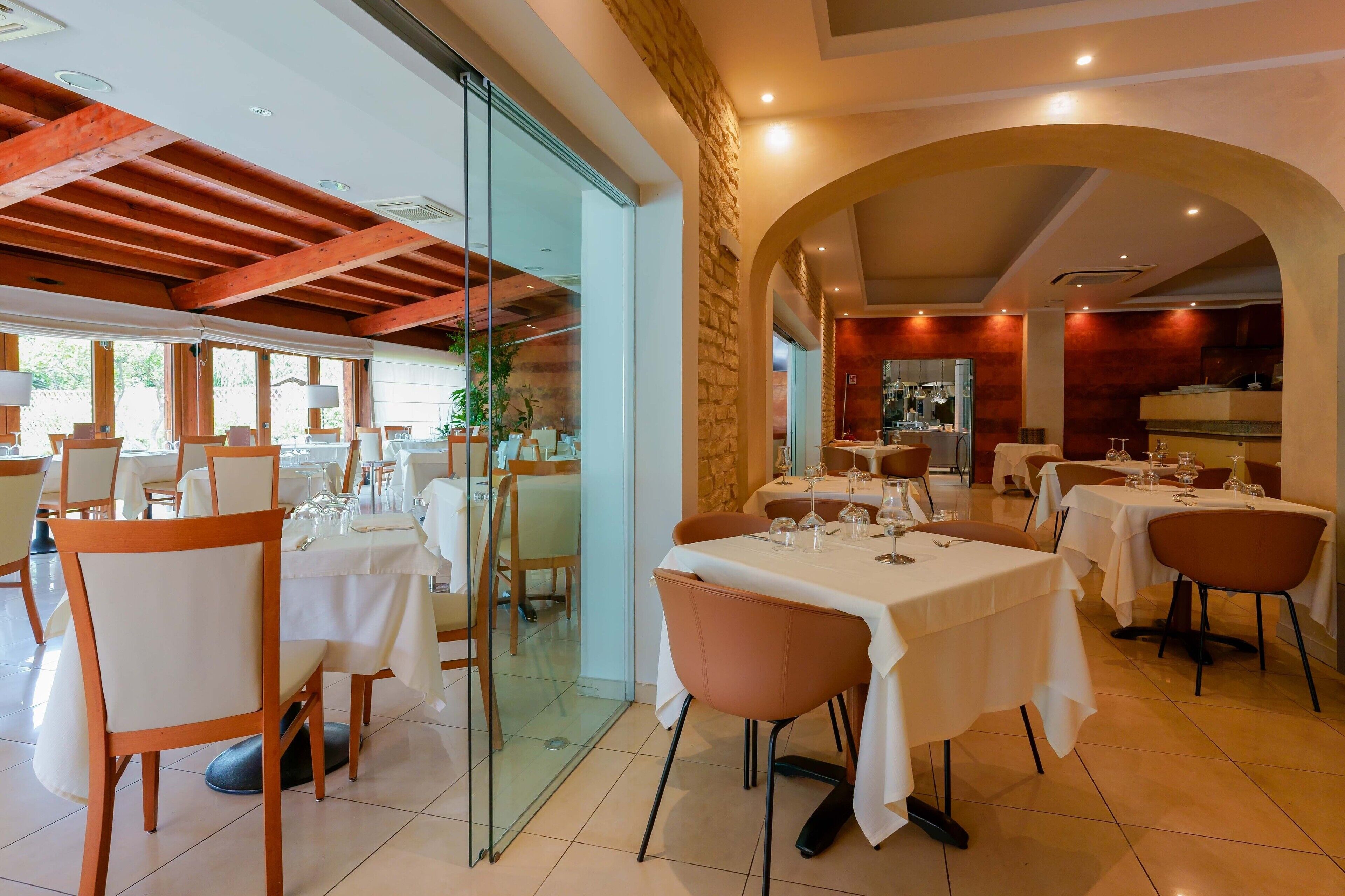 Un restaurante con mesas listas para comer, vigas de madera en el techo y una pared de piedra.