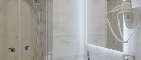 Un baño moderno con ducha de vidrio, lavamanos blanco e iluminación integrada en el espejo.