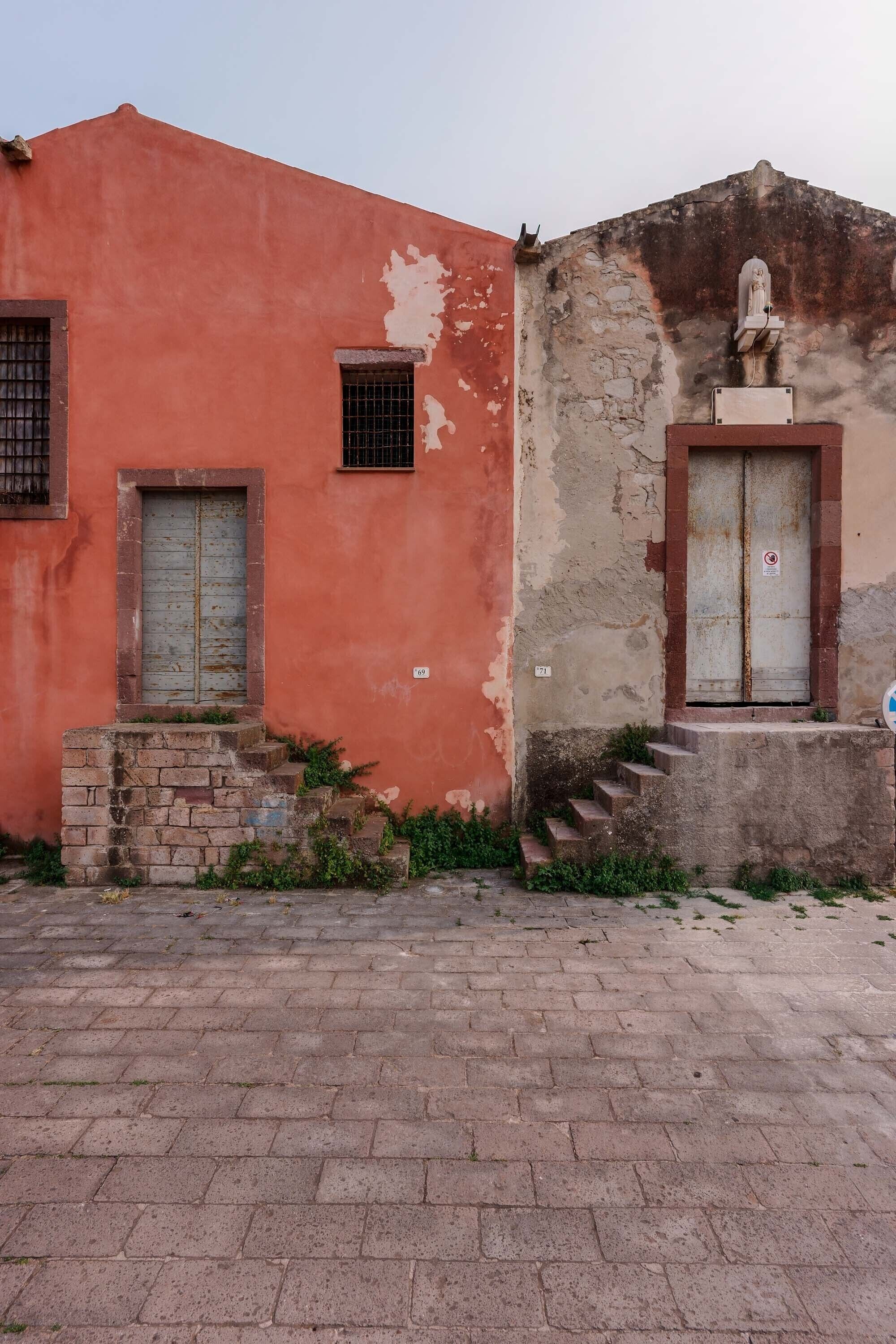 Un bâtiment à la façade rouge, avec une petite fenêtre et une statue sur le côté droit.