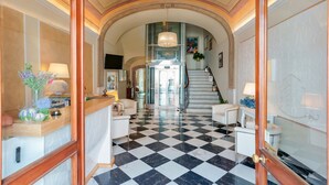 Un hall de hotel con piso a cuadros, una escalera y una zona de recepción con mostrador y asientos.