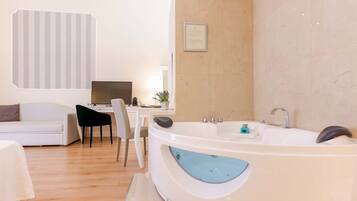 A modern bathroom with a freestanding bathtub, a white sofa, a desk with a computer, and a chair.
