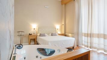 A modern hotel room with a large bed, a wooden side table with a built-in bathtub, and a large window with sheer curtains.