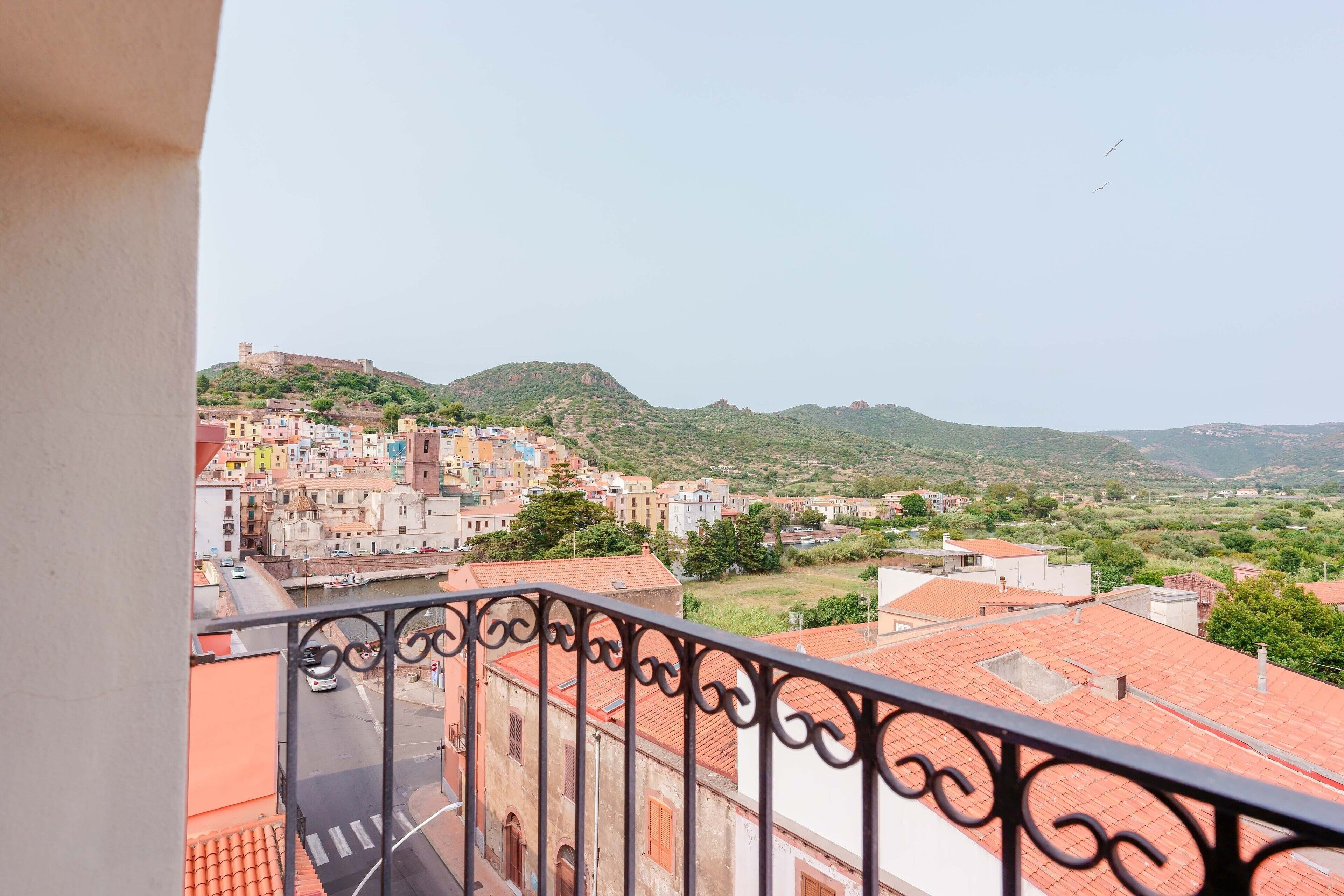 A balcony with a view of a town, including buildings and a hill with a tower.