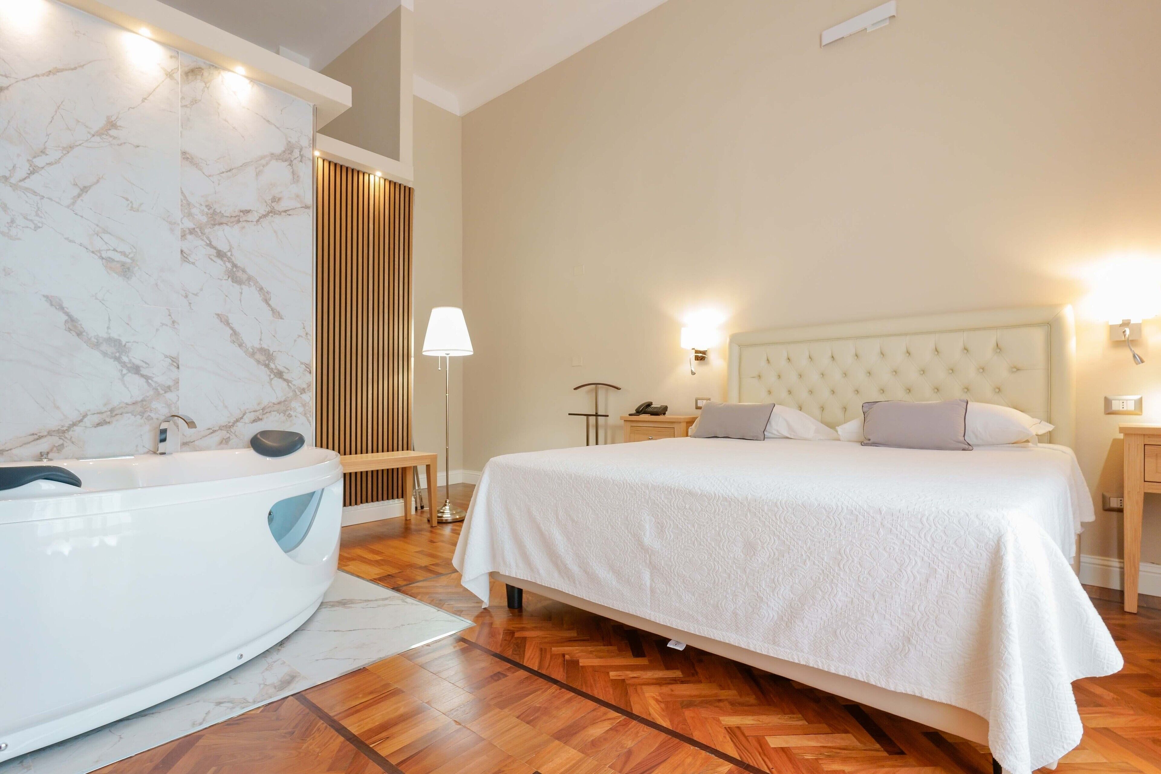 A modern hotel room with a marble bathroom, a large bed with a tufted headboard, and wooden flooring.