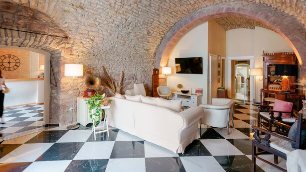 Un amplio salón con suelo a cuadros, un sofá blanco y una pared de piedra.