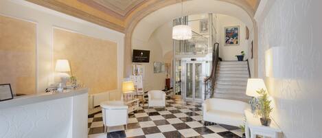 Un vestíbulo con piso a cuadros, muebles blancos, una recepción y una escalera que lleva a los pisos superiores.