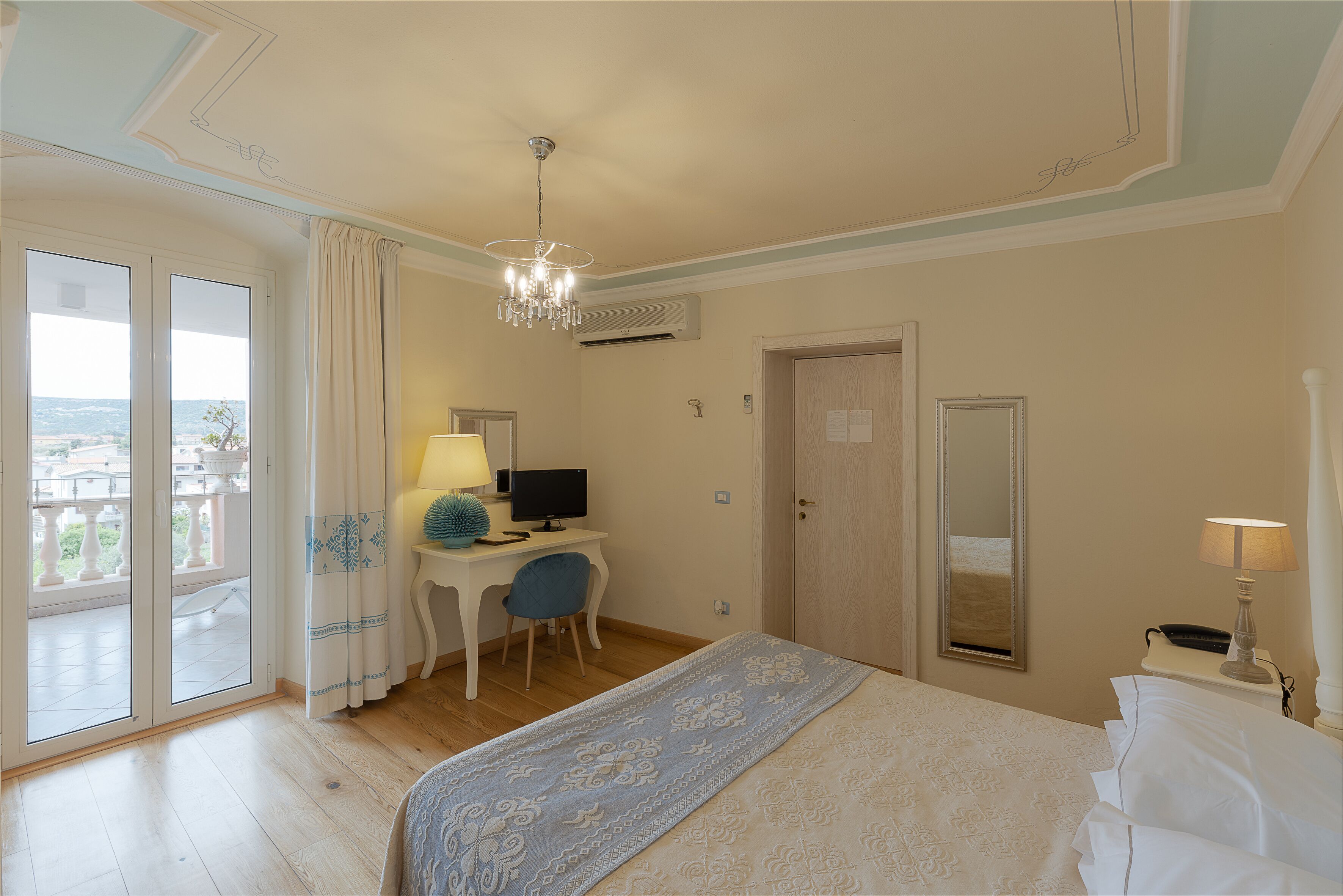 Ein Hotelzimmer mit Bett, Schreibtisch mit Computer, Stuhl, Lampe und einem großen Fenster mit Vorhängen.